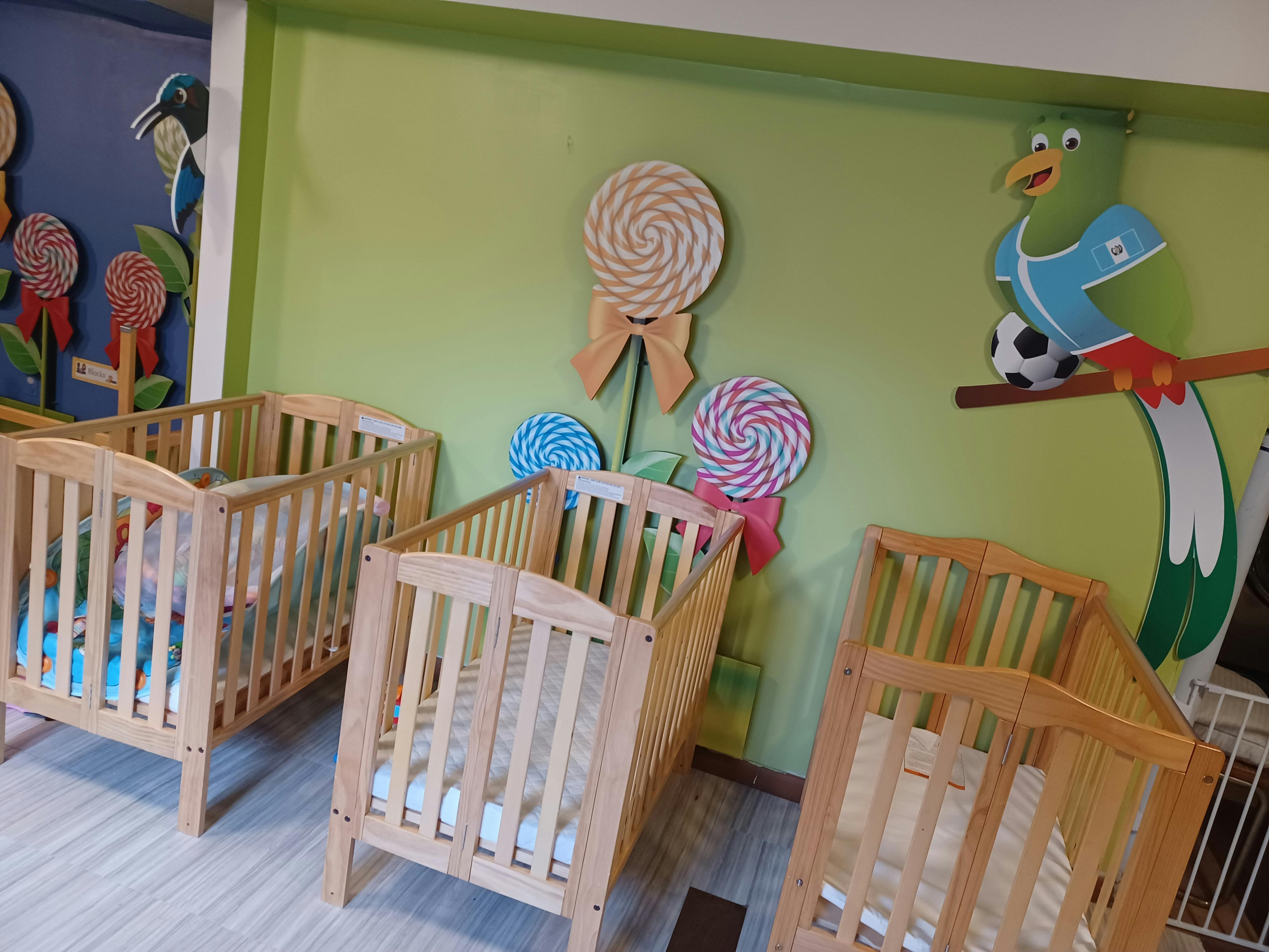 Three wooden cribs in a room with colorful wall decorations