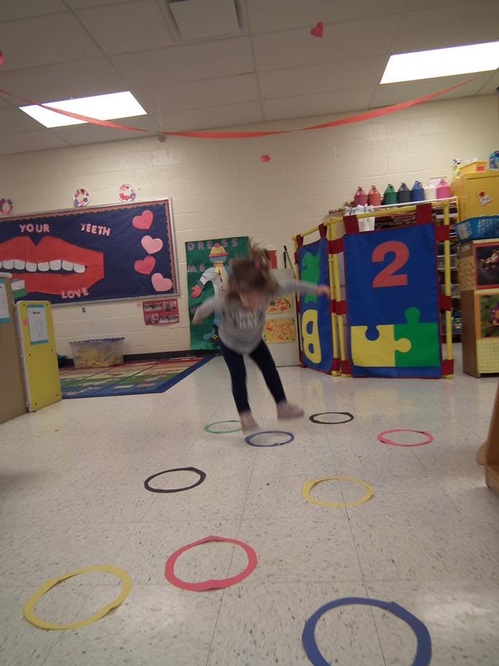 Child jumping on colorful rings on the floor in a classroom