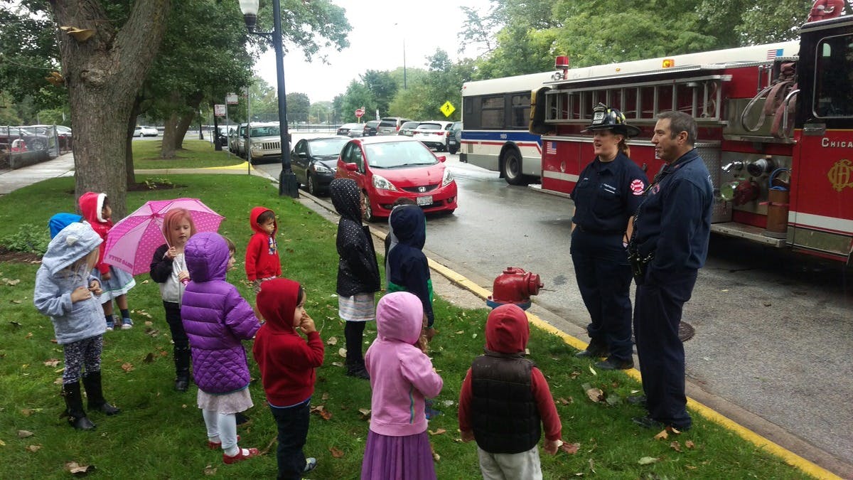 Children gathered around two people in uniform next to a fire truck