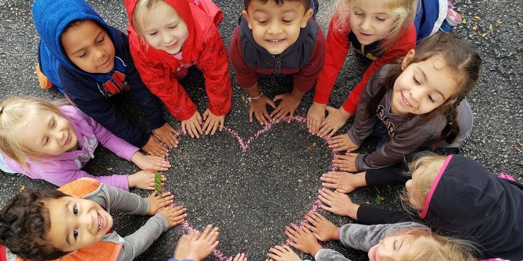 Children forming a heart shape with their hands on the ground
