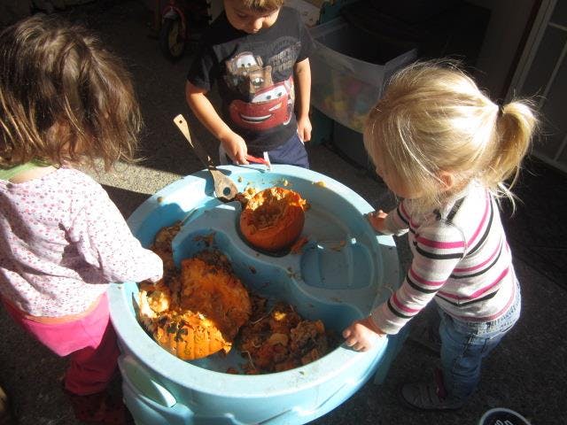 Three children playing with pumpkins in a blue water table