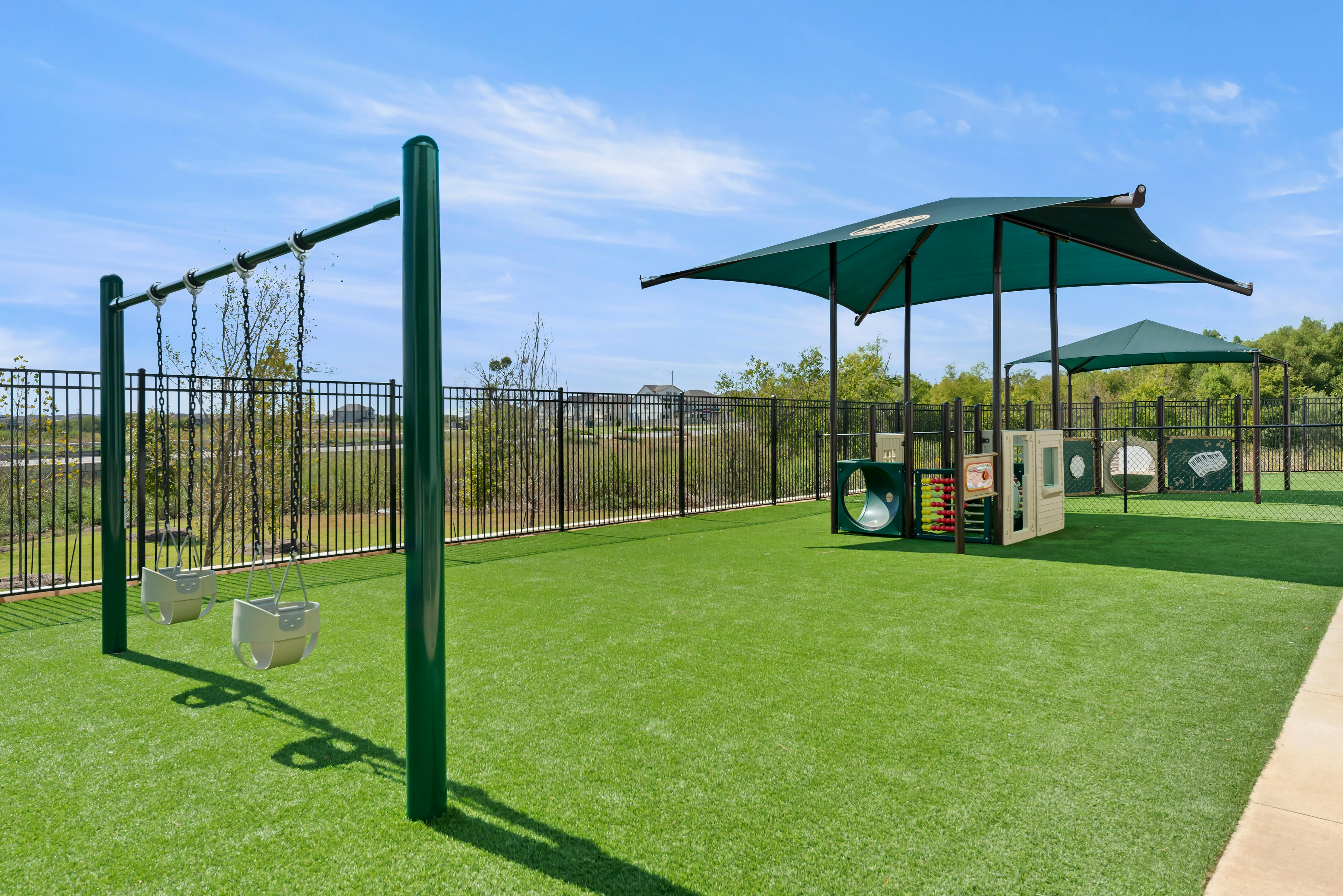 Outdoor playground with green turf, baby swings, and shaded play structures