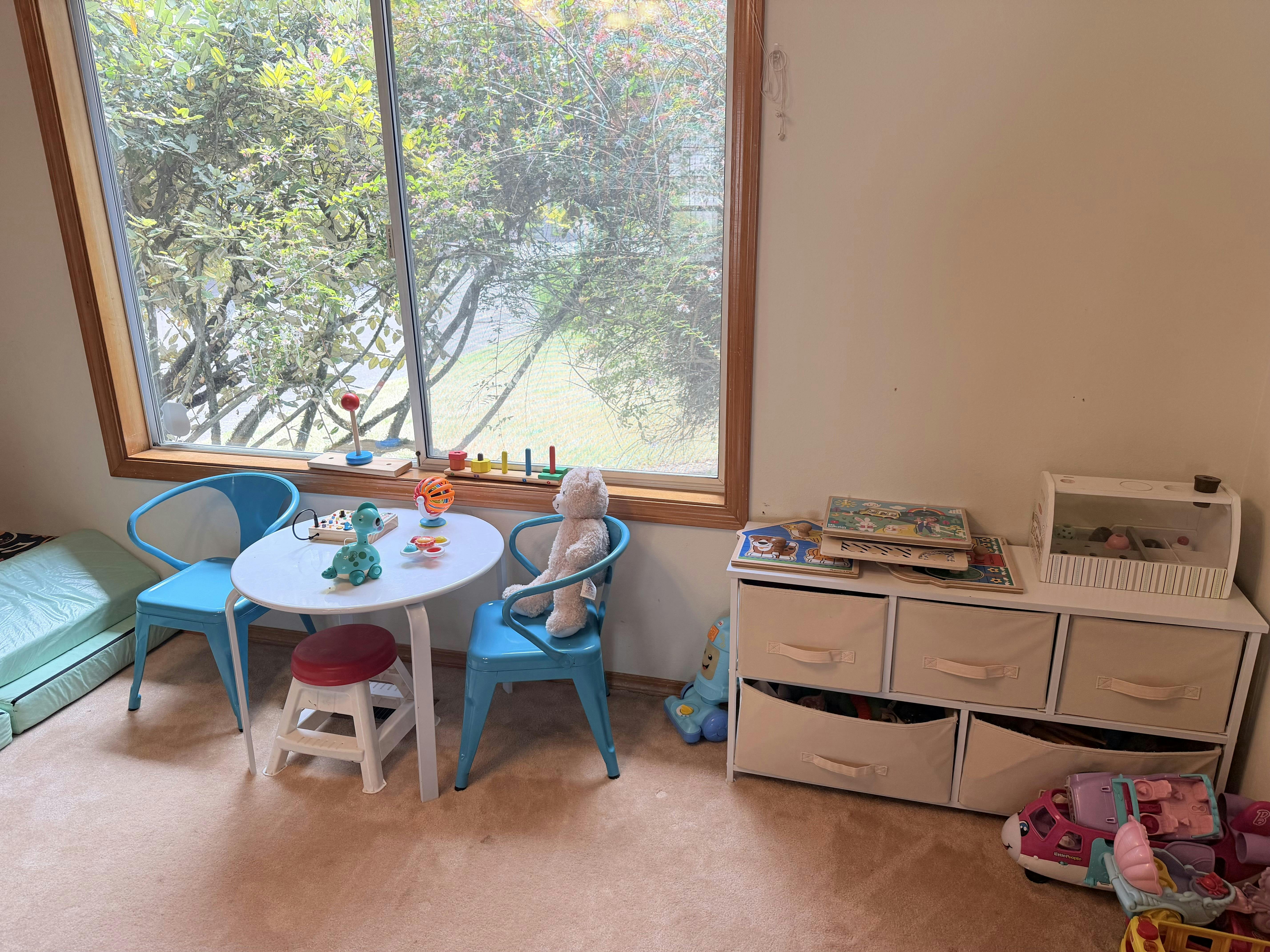A children's playroom with a small table, blue chairs, and toy storage