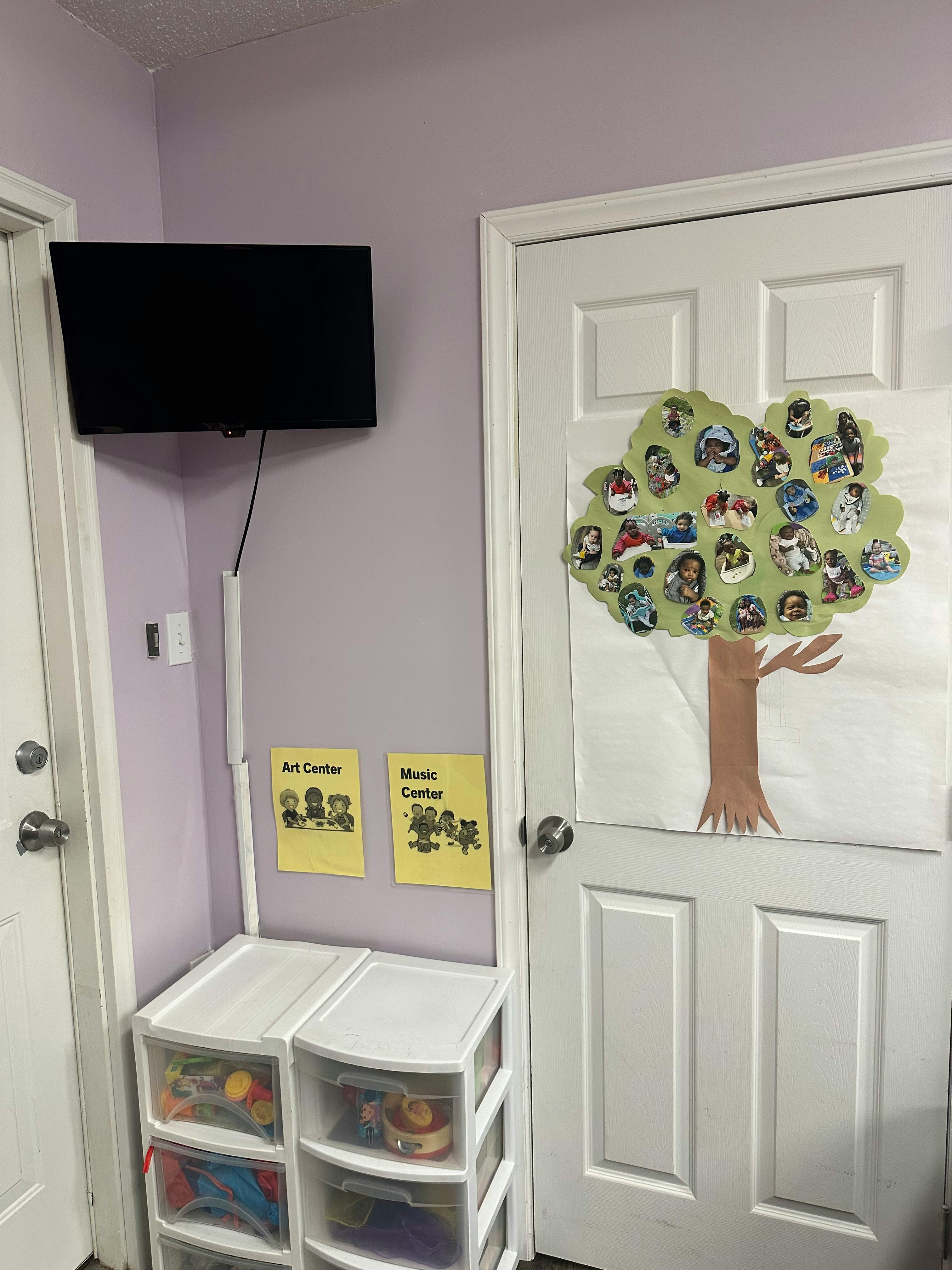 Wall-mounted television above plastic storage drawers and a door with a paper tree