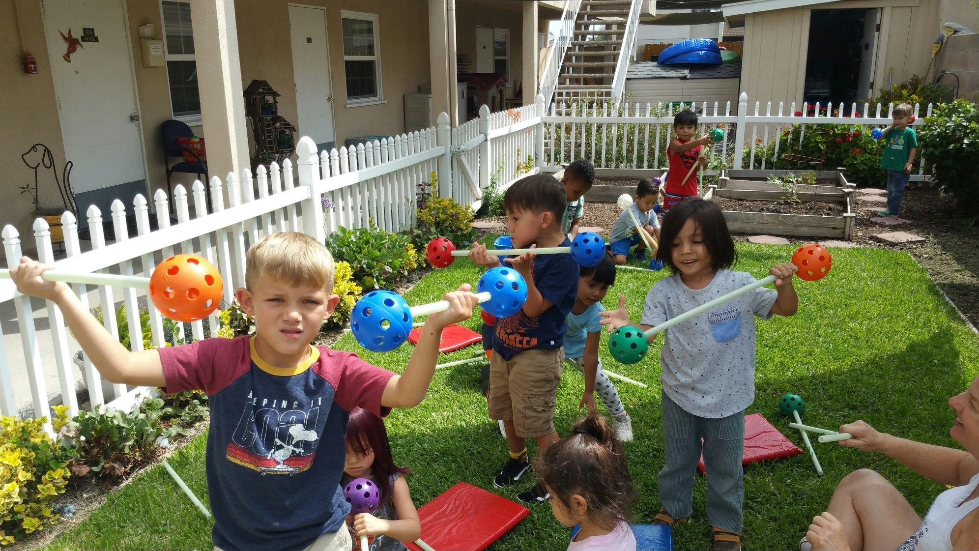 Children playing with colorful balls on sticks in a grassy yard