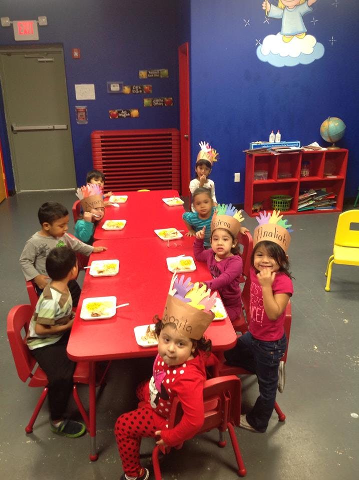 Children wearing paper hats sitting at a red table in a classroom