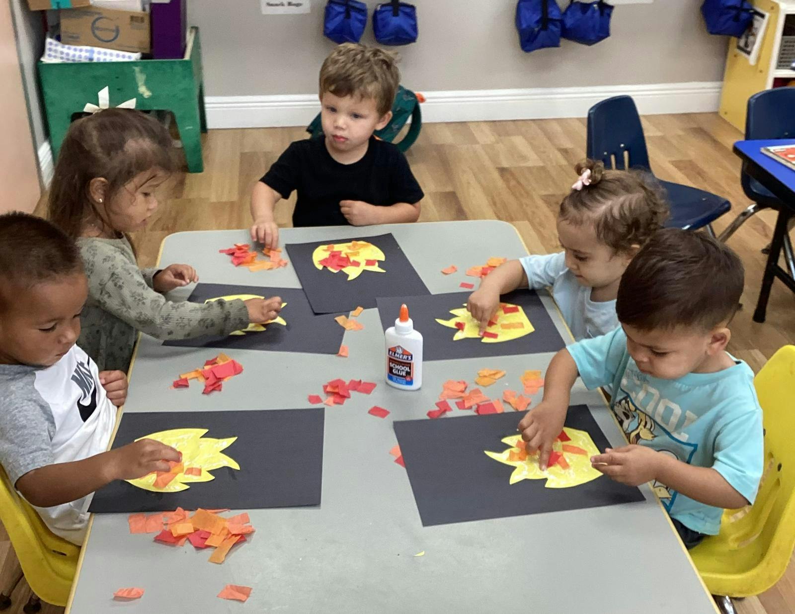 Group of children working on paper crafts at a table in a classroom