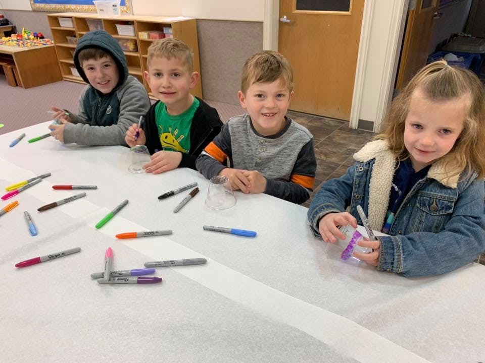 Four children sitting at a table with markers