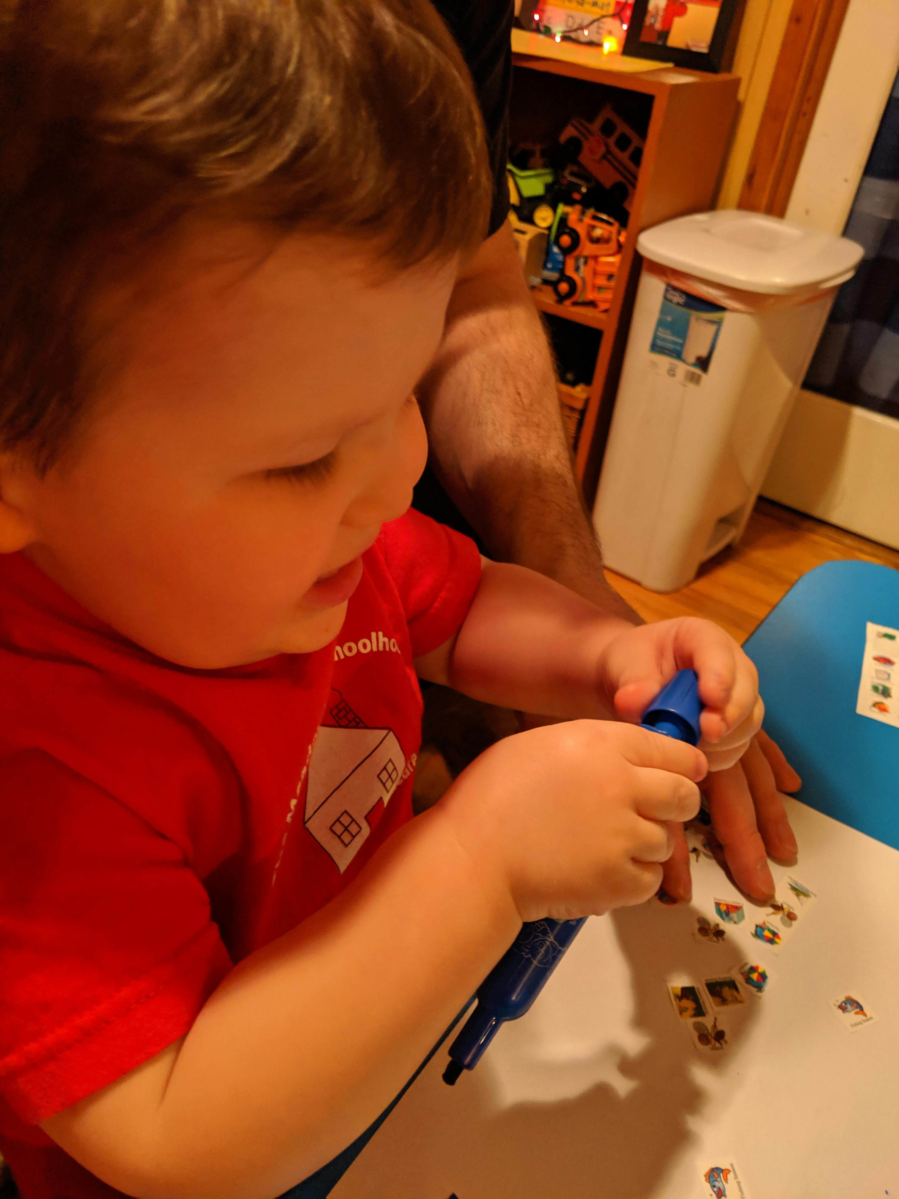 Child in red shirt holding a blue marker over-sized crayon