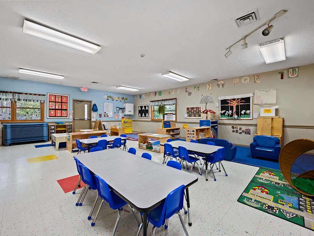 Empty classroom with small tables and chairs, and play areas