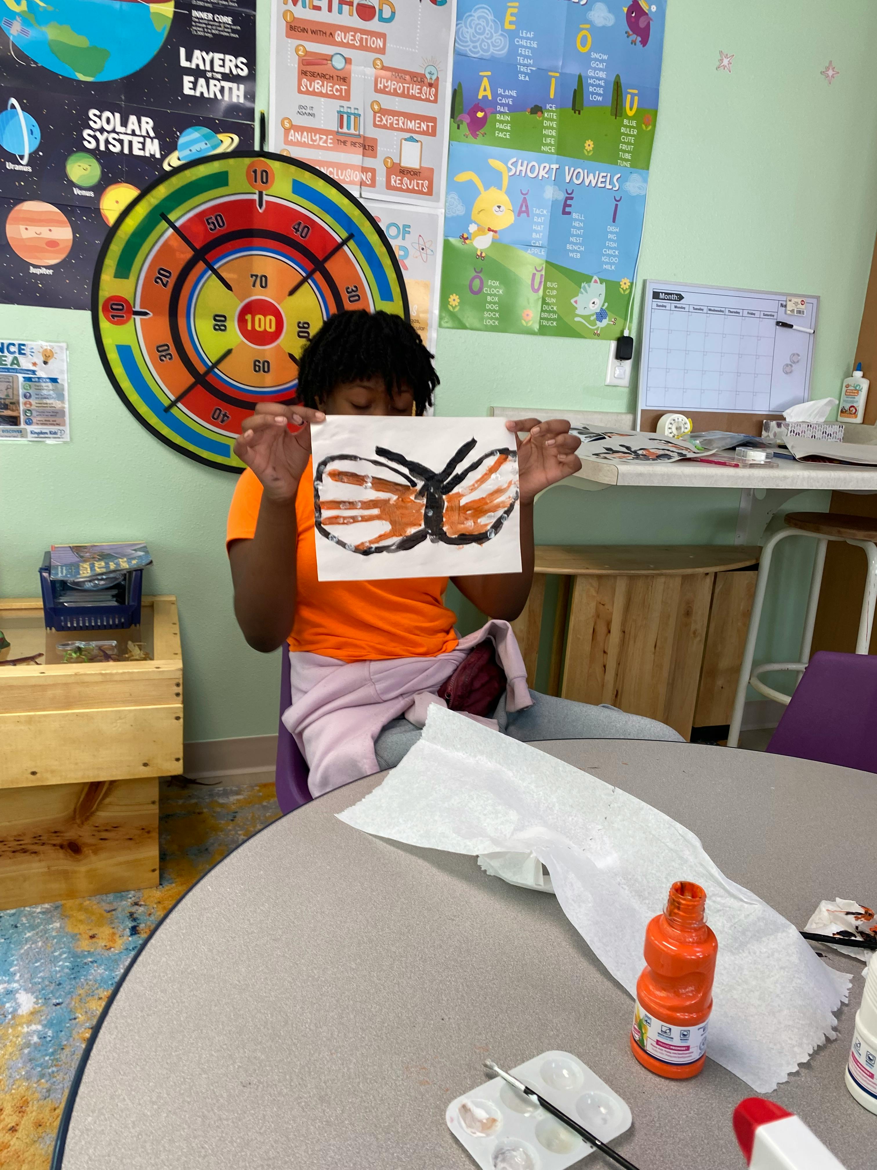 Child holding up a handprint painting of a butterfly