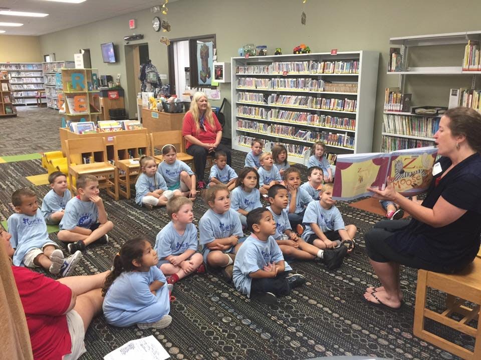 Adult reading a book to a group of children sitting on the floor in a library