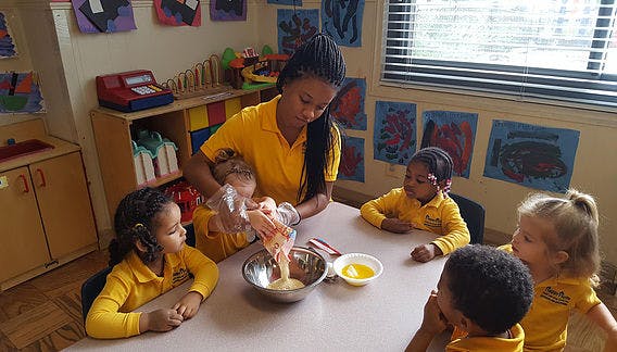 Person helping children mix ingredients in a bowl at a table