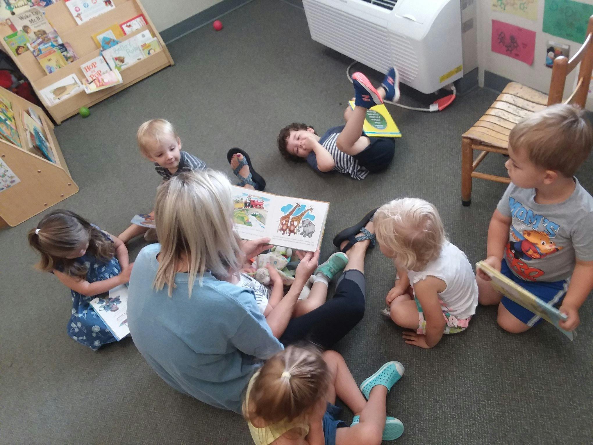 Person reading a book to multiple children on the floor