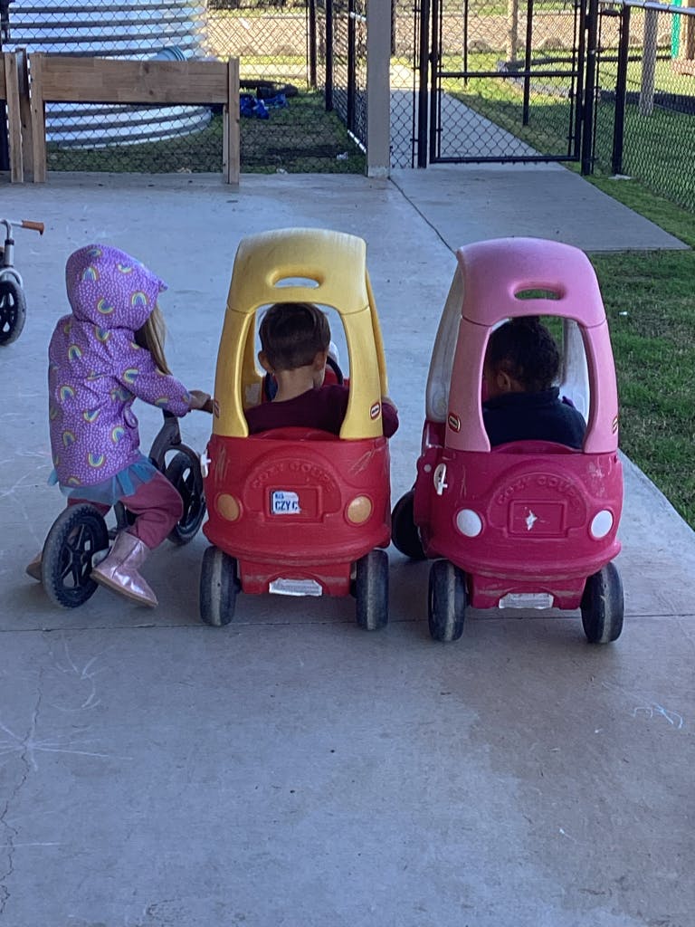 Child on a tricycle next to two children in toy cars