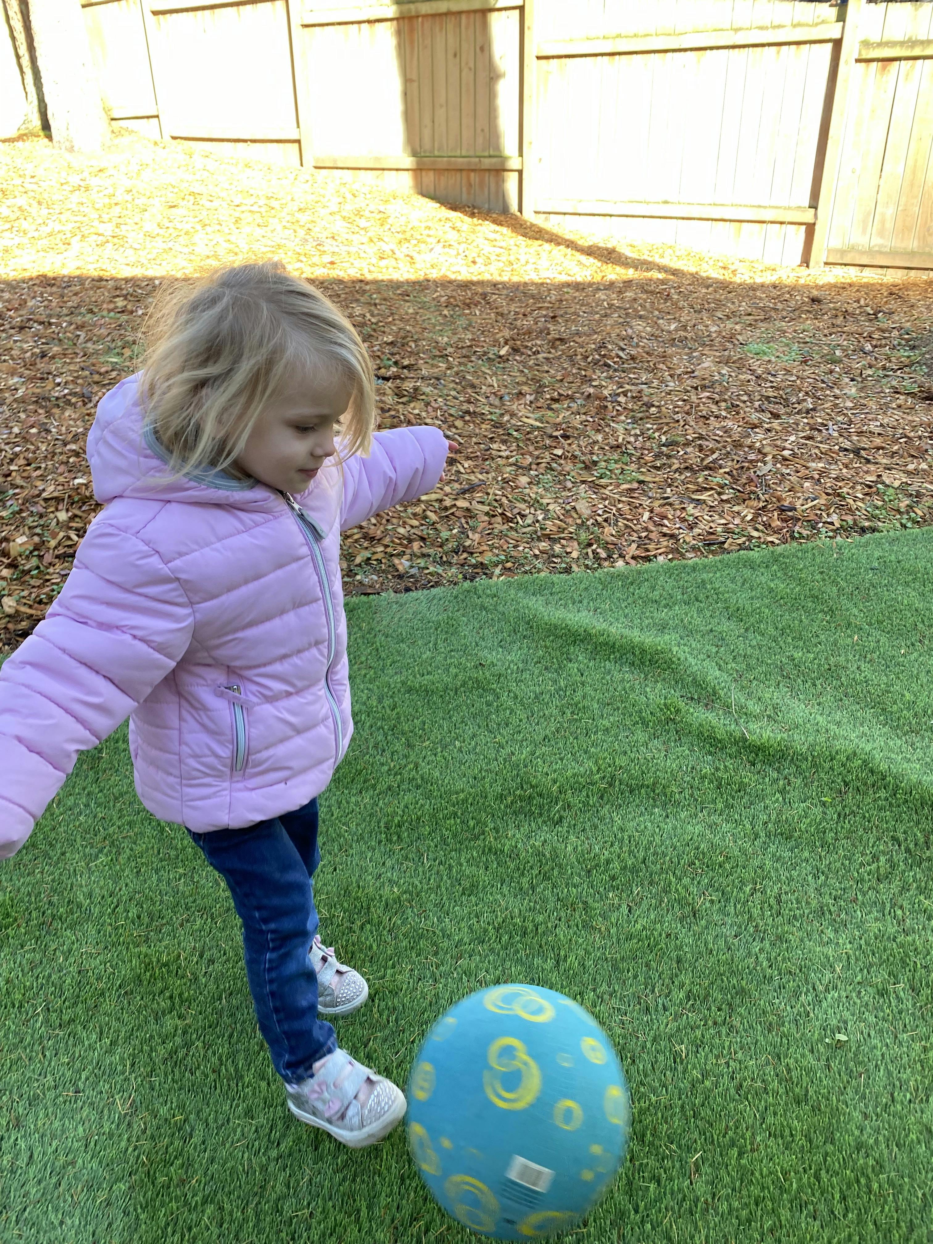 Child kicking a blue ball on green turf