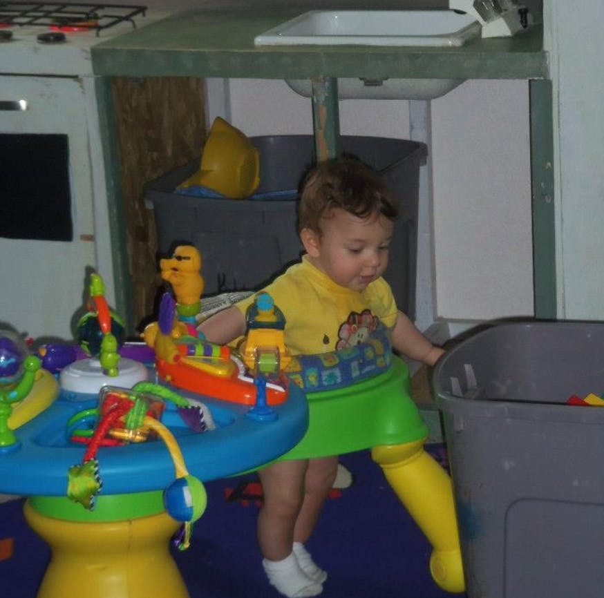 Child in a play saucer reaching into a bin