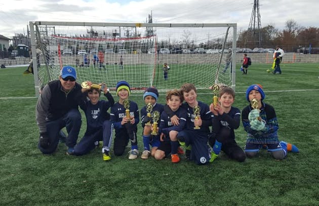 Adult and children kneeling on a soccer field with trophies