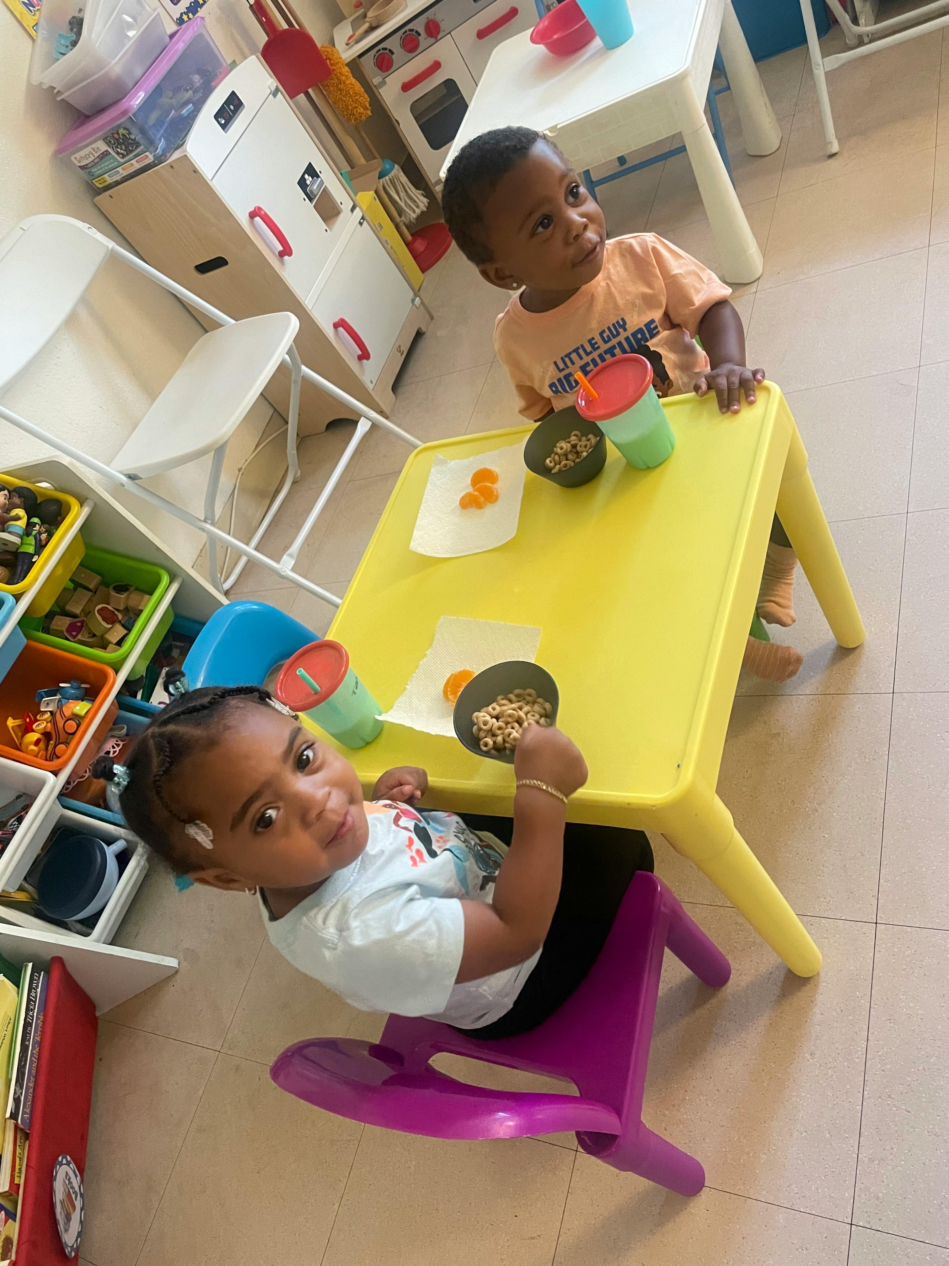 Two children sitting at a yellow table with snacks