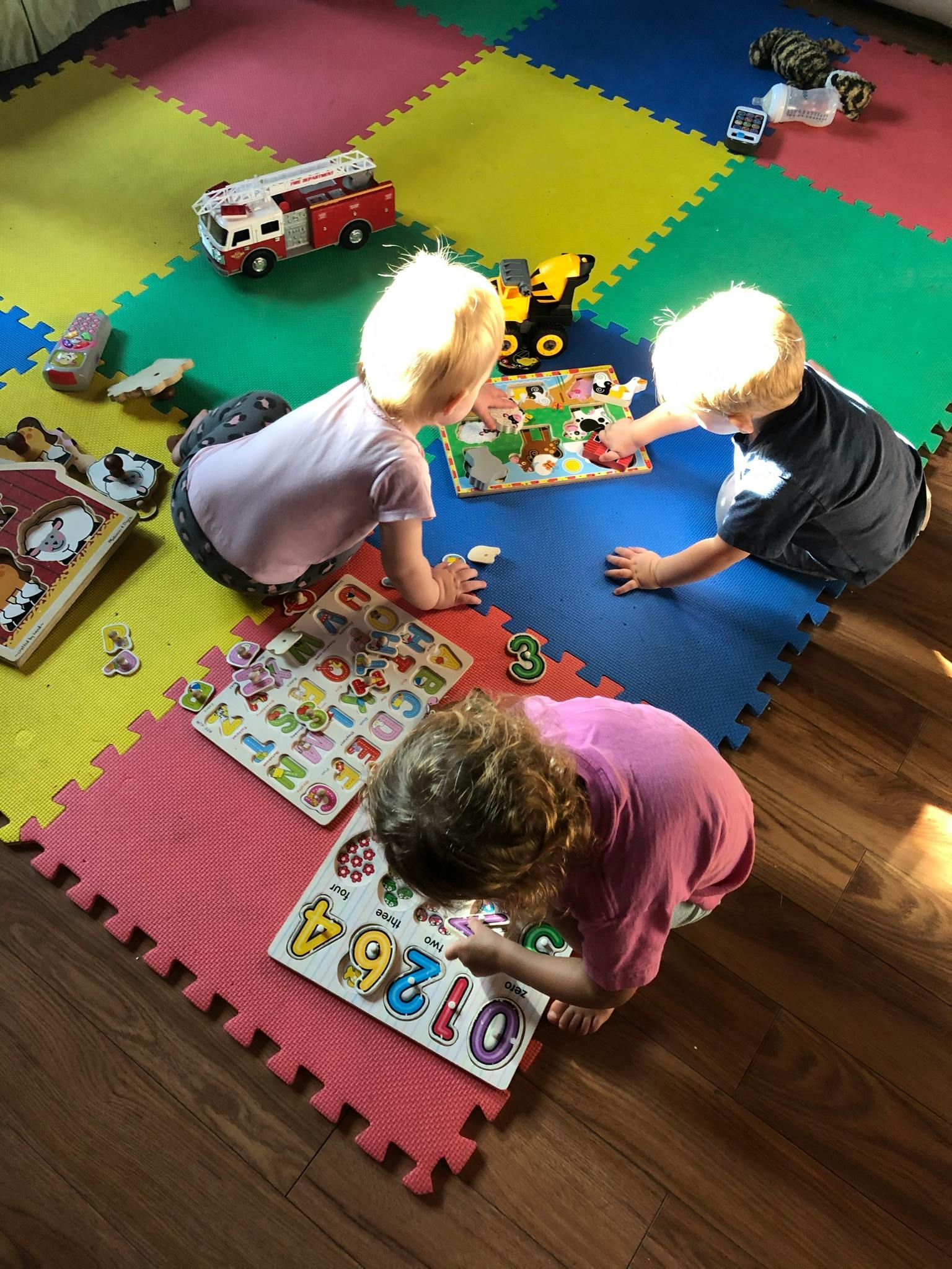 Three children playing with puzzles on a colorful mat