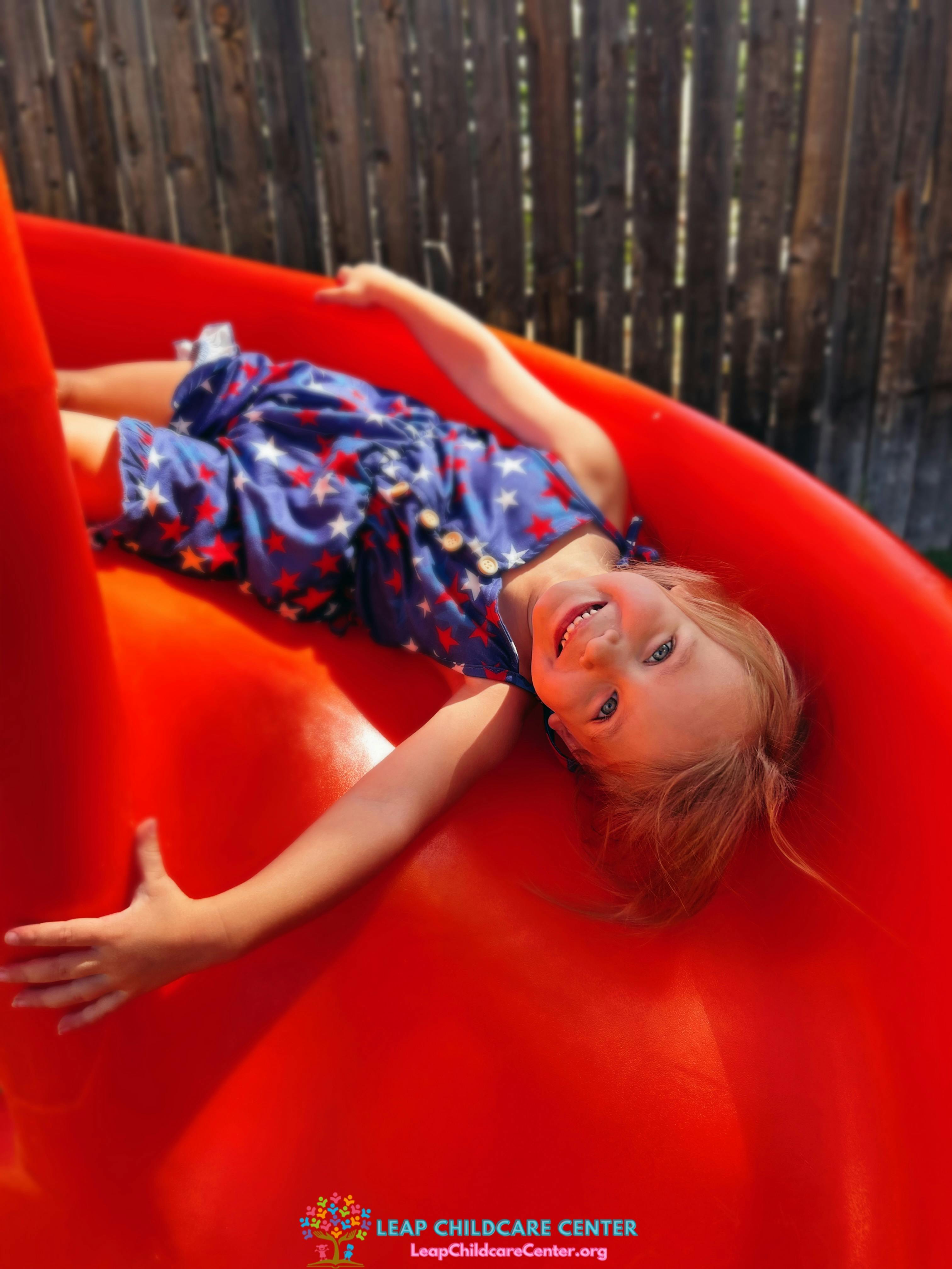 Child in a star-patterned outfit lying on a red slide