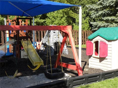Playground with swings, slide, and playhouse under a blue canopy