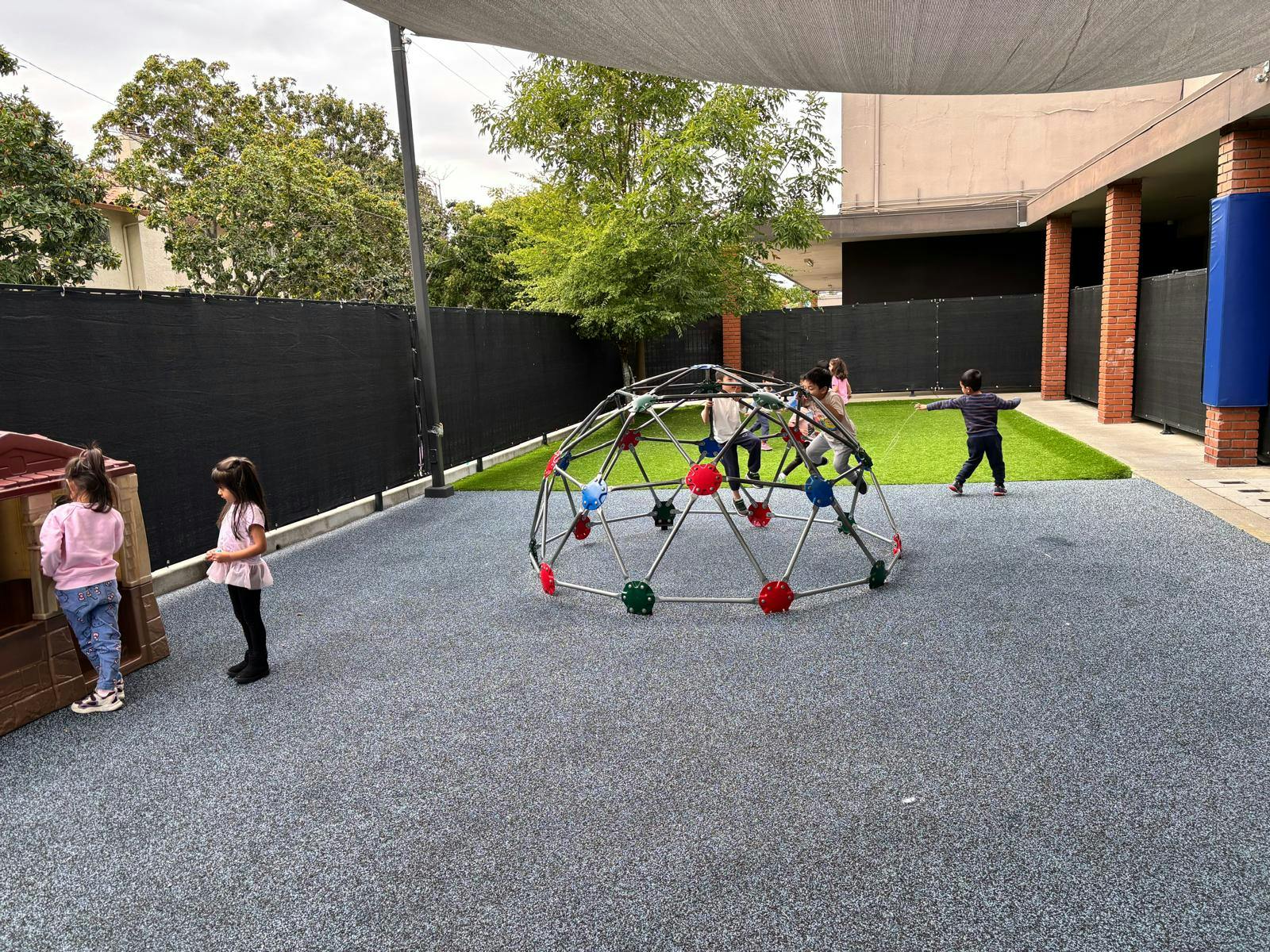 Children playing on a geodesic dome climber and a playhouse on a playground