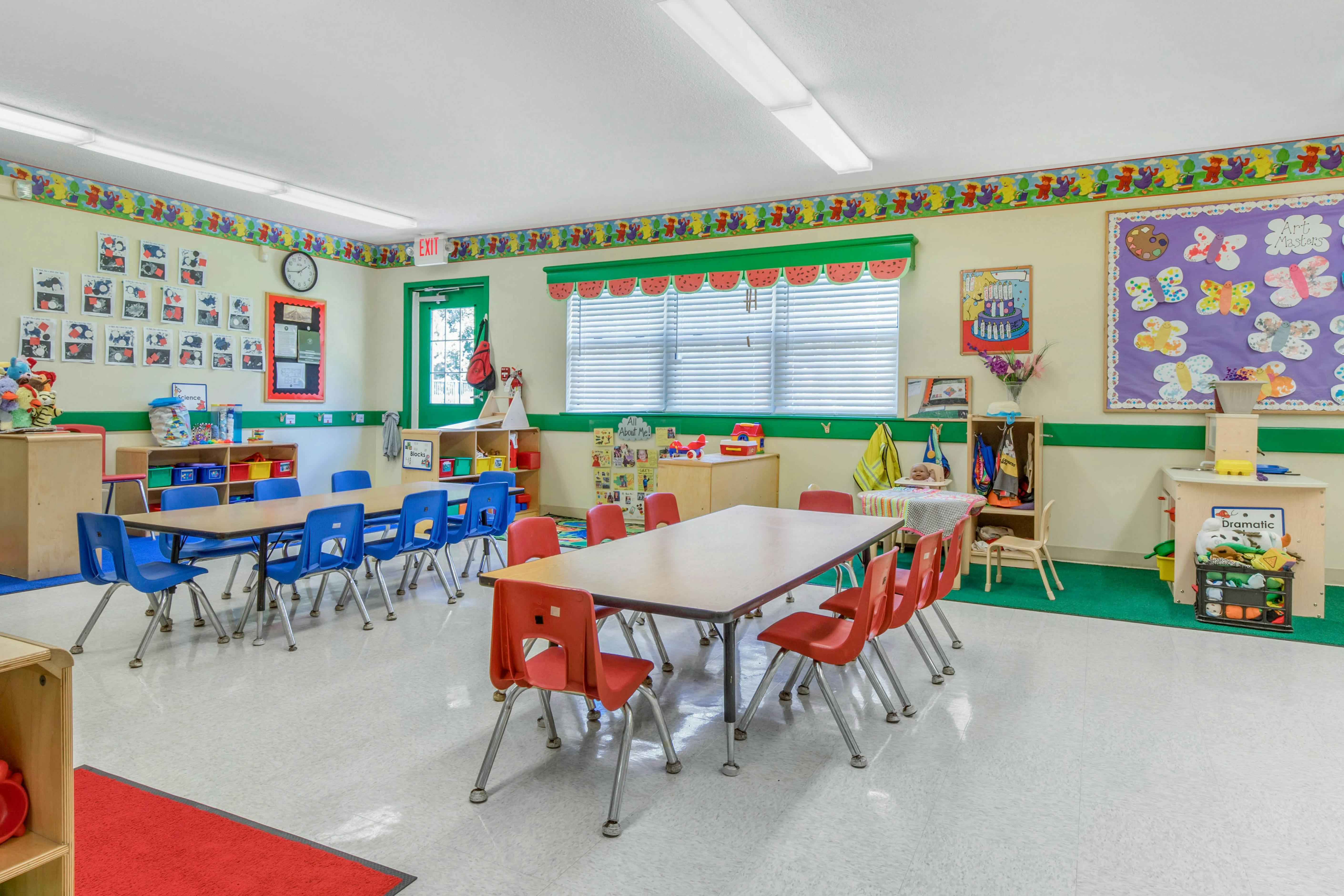 An empty classroom with two tables and small chairs, artwork on the walls