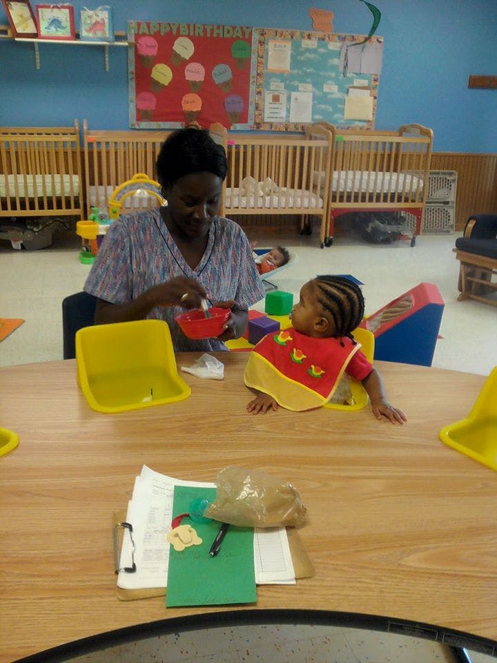 Person feeding a child in a high chair at a table