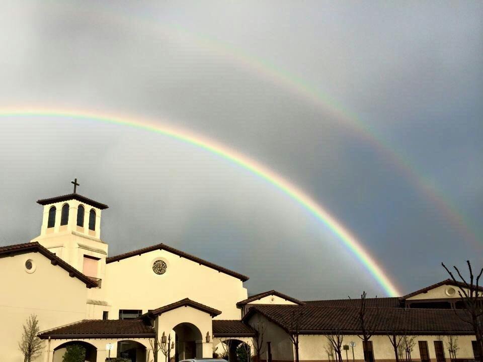 Building with a cross on top and a double rainbow in the sky