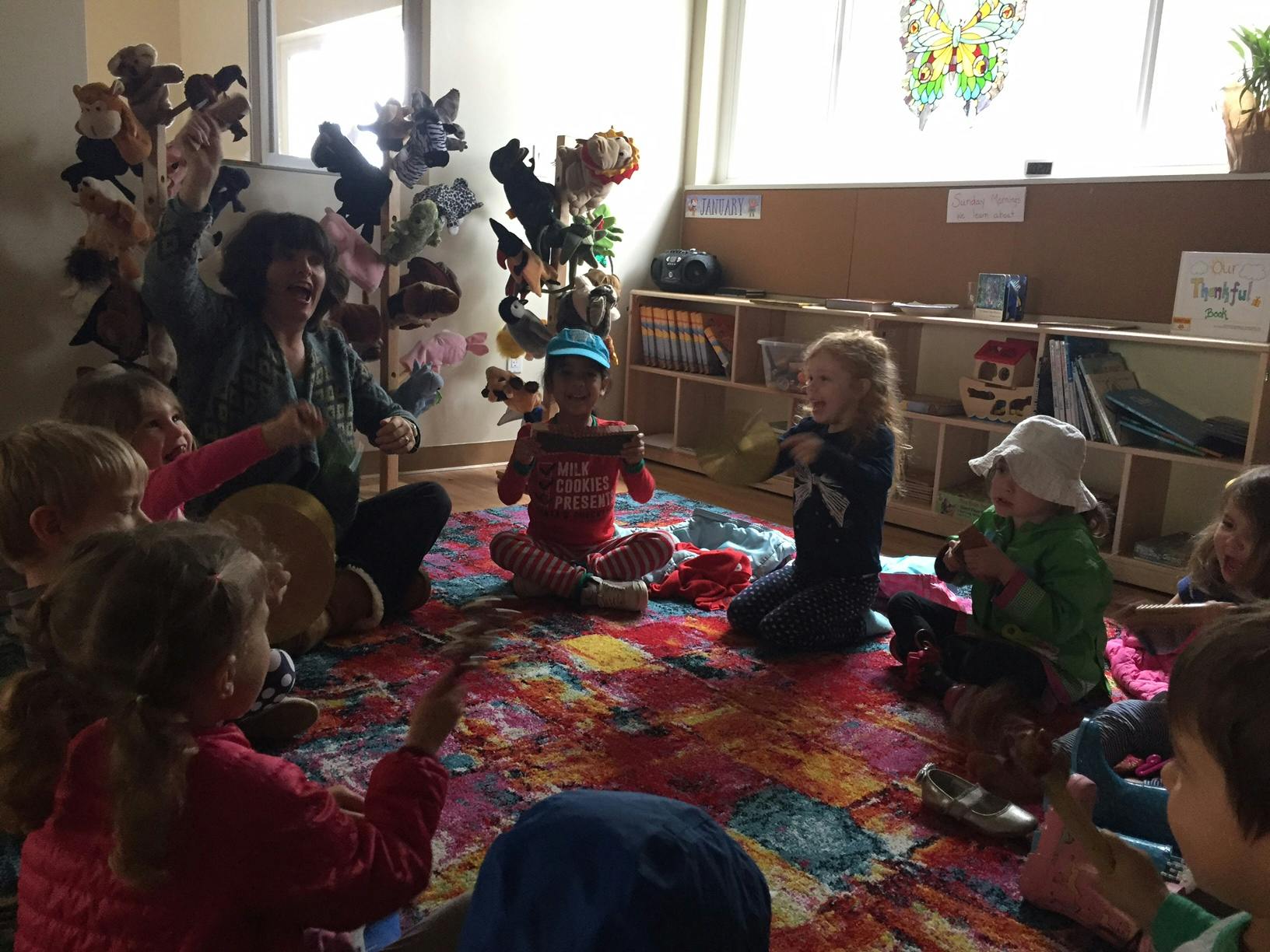 Adult and children sitting on a colorful rug in a classroom