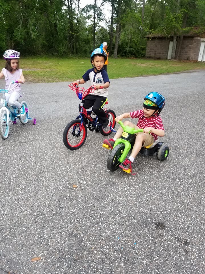 Three children riding bicycles and a tricycle outdoors