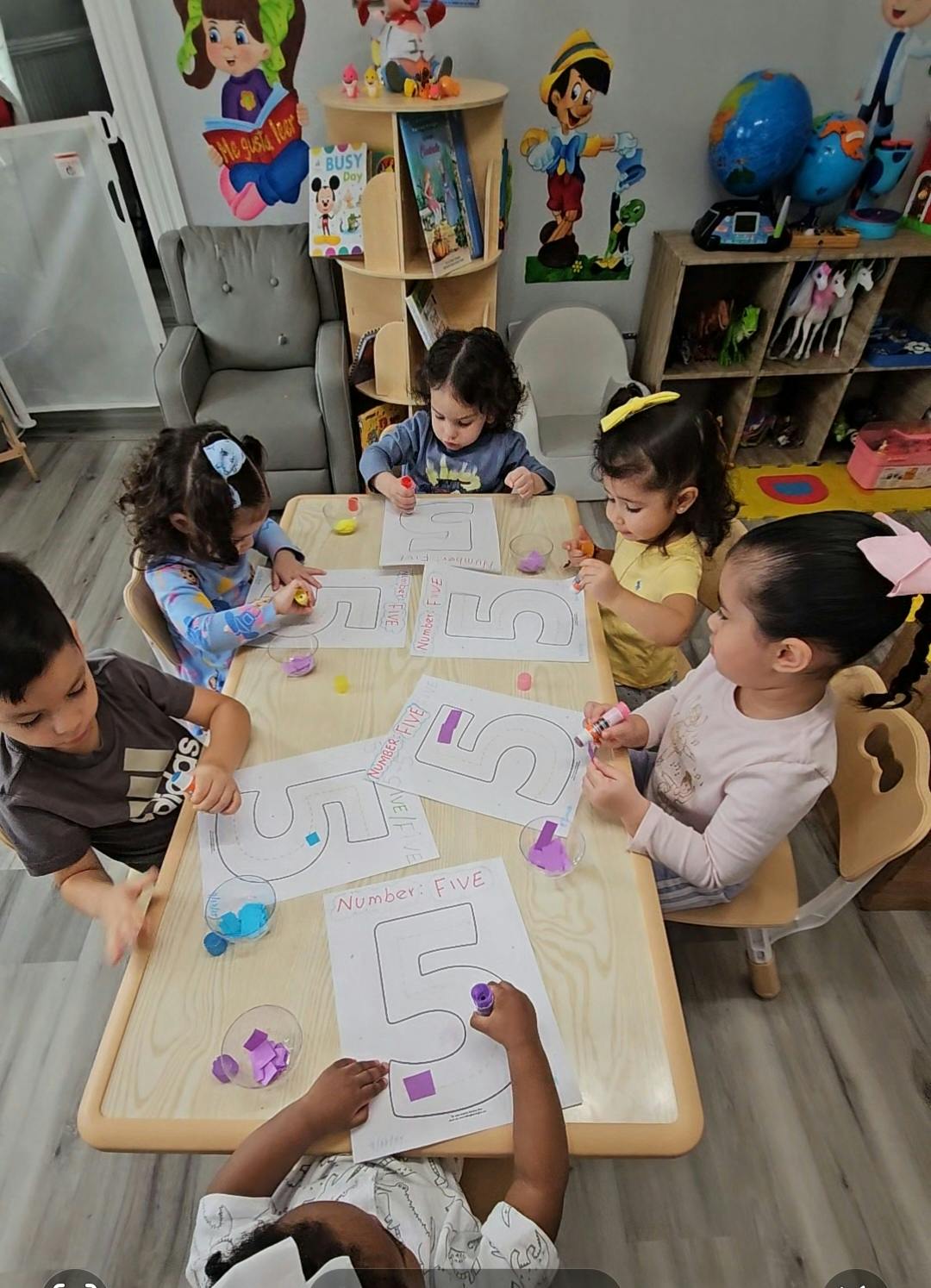 Five children doing a number tracing activity at a table