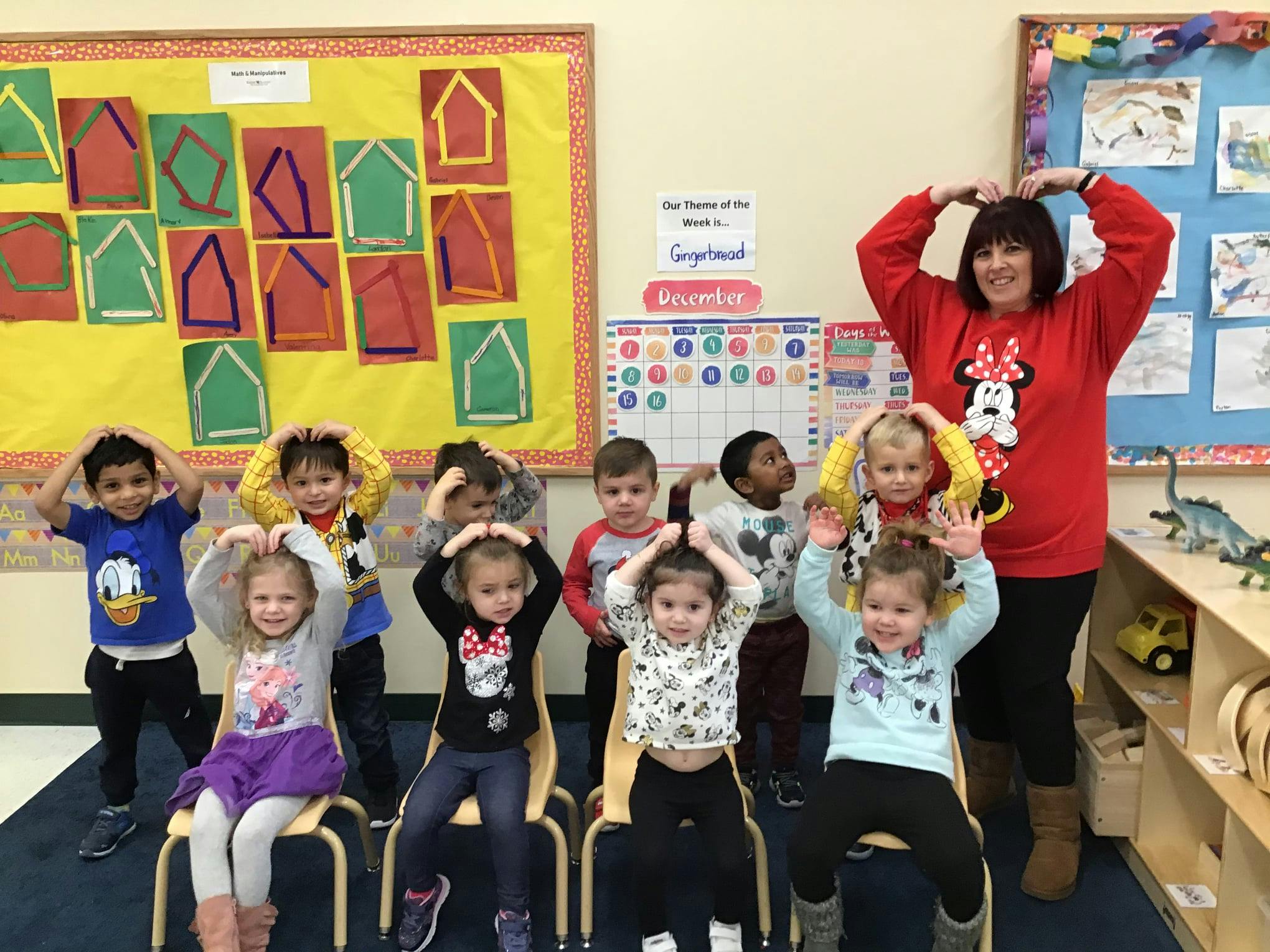 Adult and children posing with hands on heads in a classroom