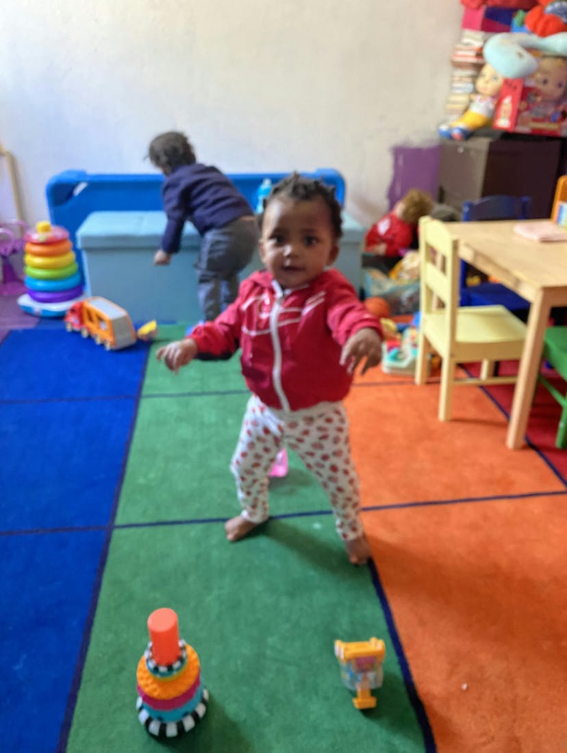 Child standing on a colorful rug with another child in the background
