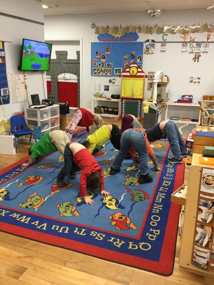 Children in a classroom doing a downward dog yoga pose on a rug