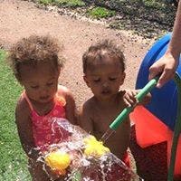 Two children playing with water from a hose