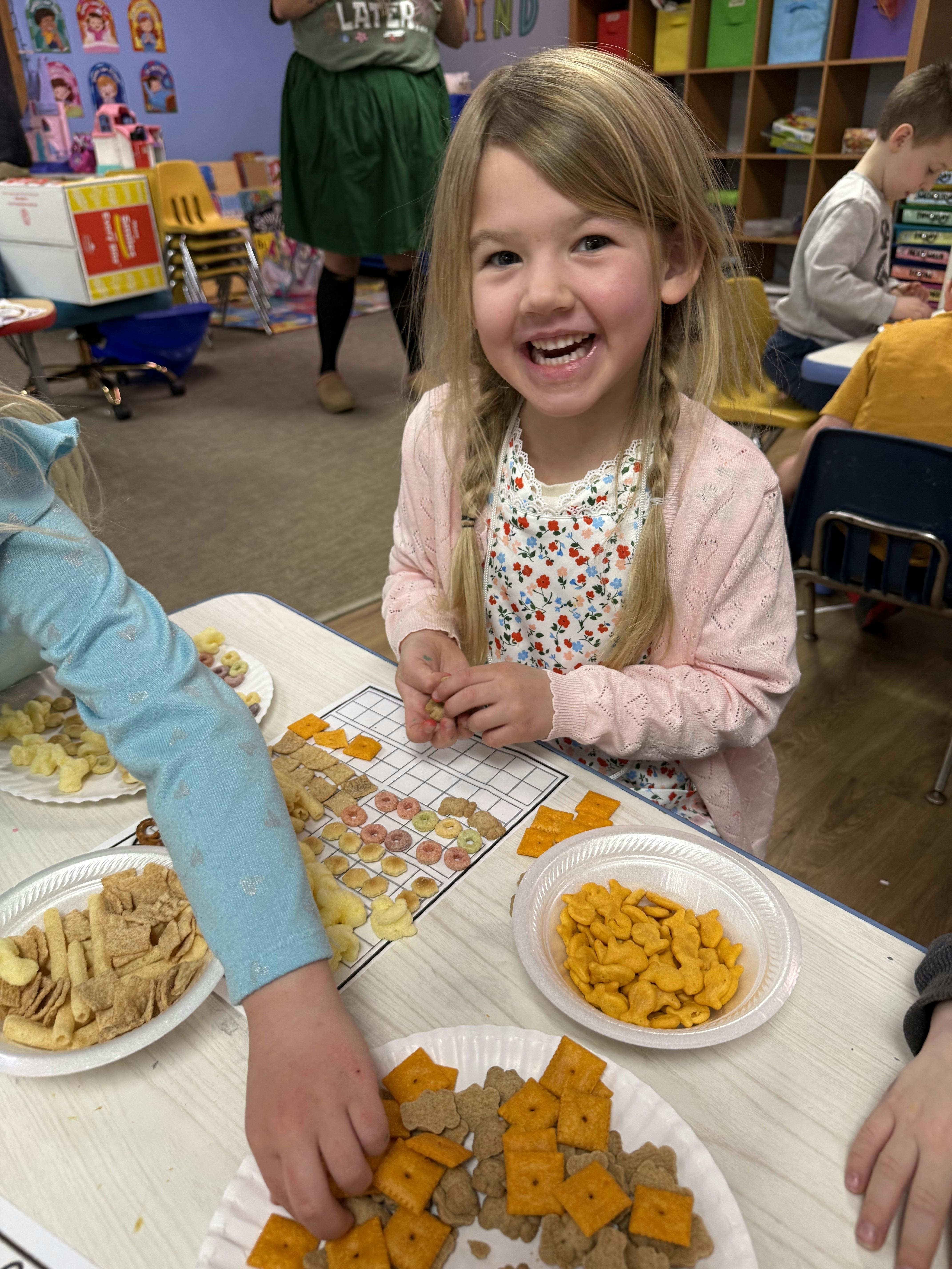 Child smiling while sorting snacks on a grid in a classroom