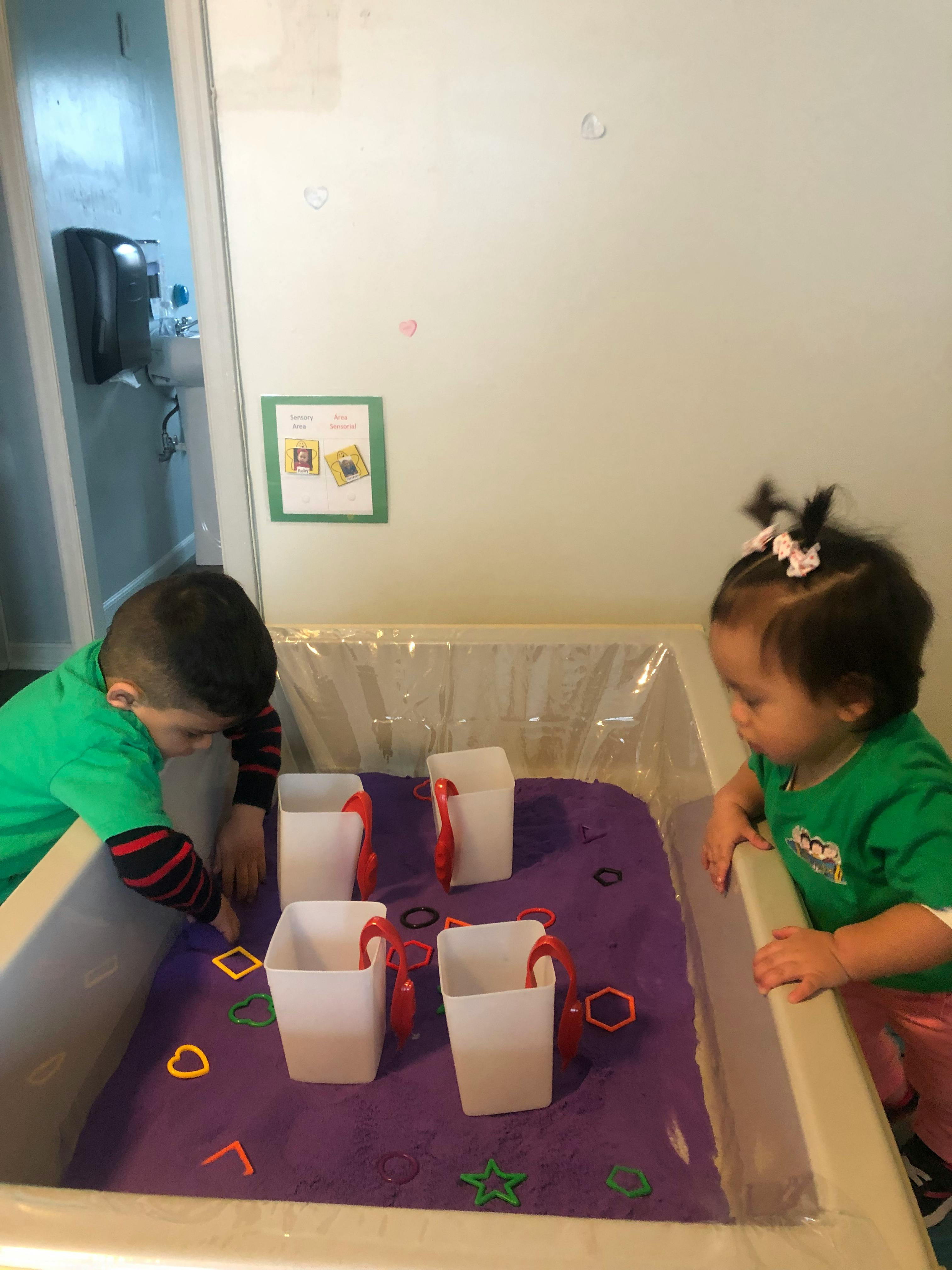 Two children playing with cups and shapes in a sensory bin