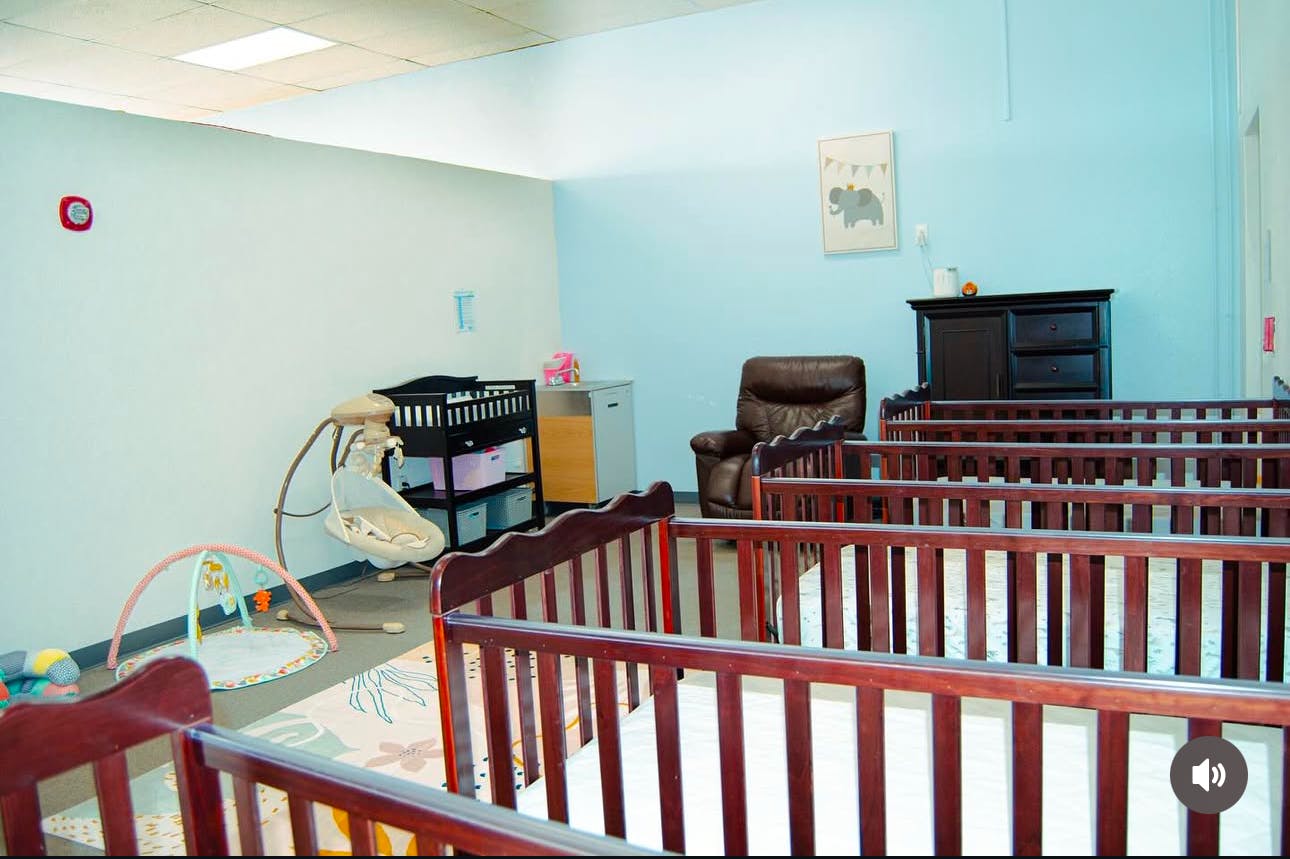 Room with multiple cribs, a baby swing, and a play mat