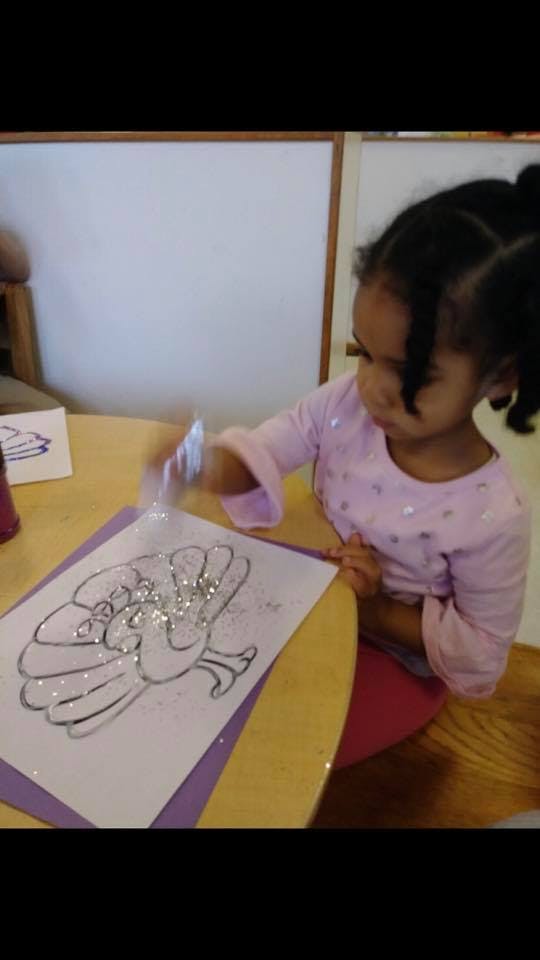 Child applying glitter to a drawing of a turkey