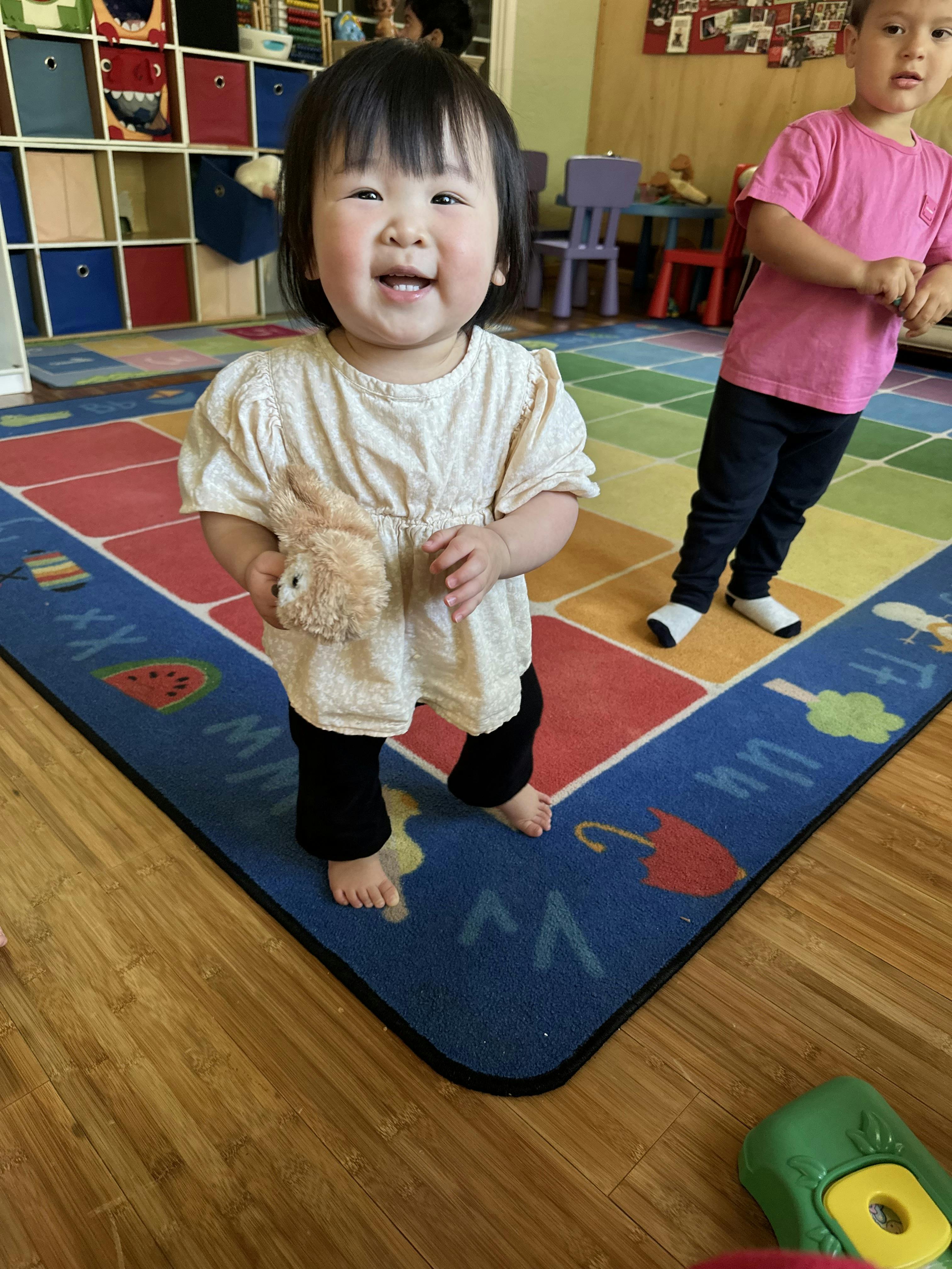 Child standing on a colorful rug, holding a stuffed animal