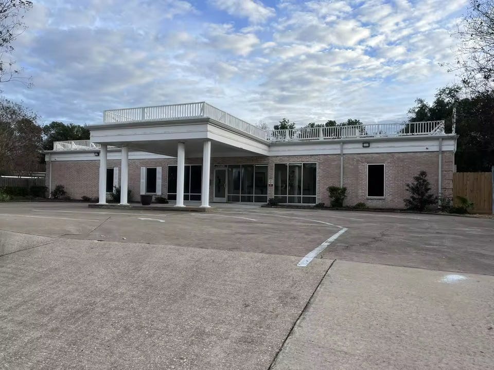 Single-story brick building with a columned portico and a rooftop railing