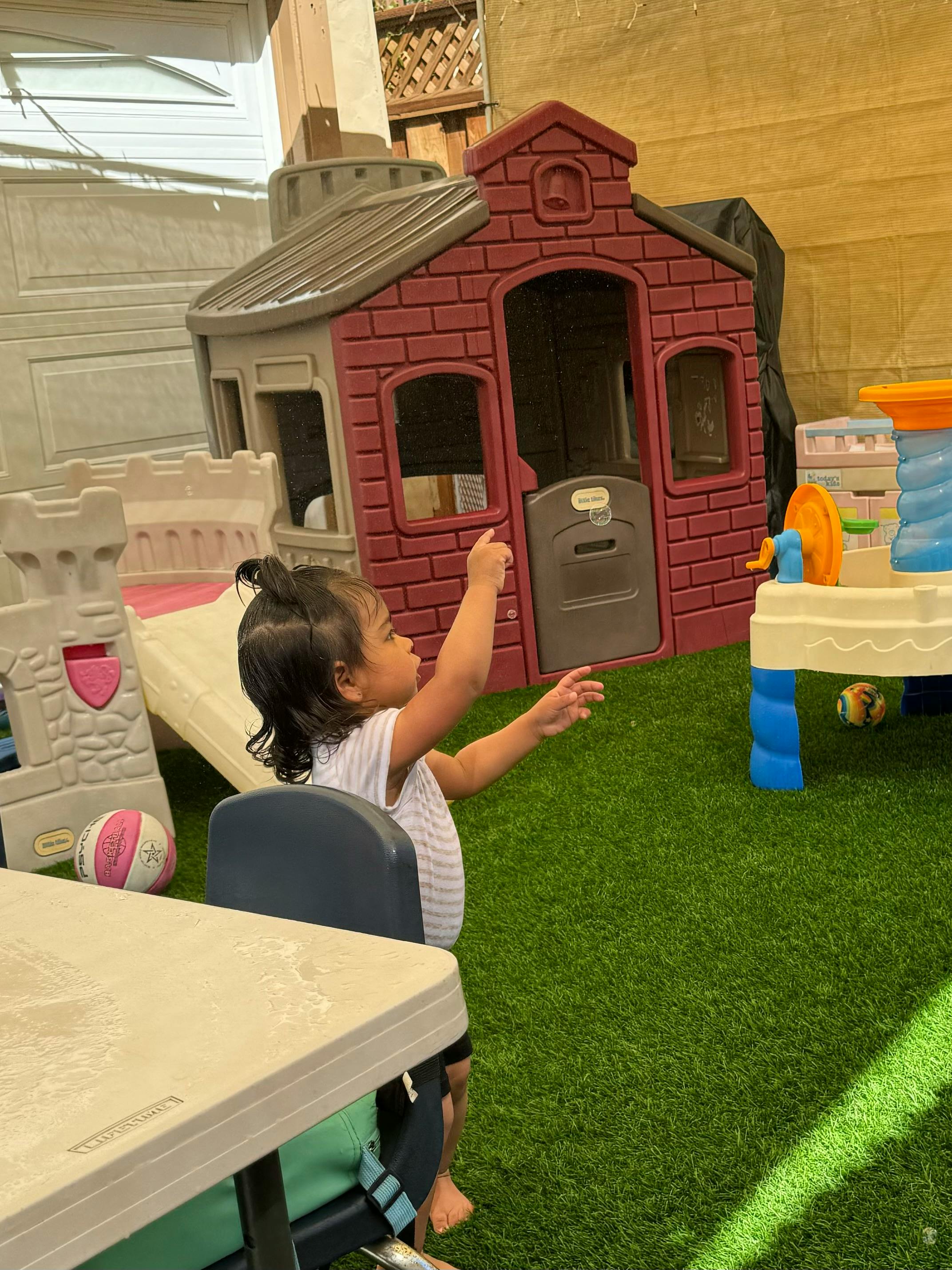 Child sitting in a chair with arms raised, pointing towards a playhouse
