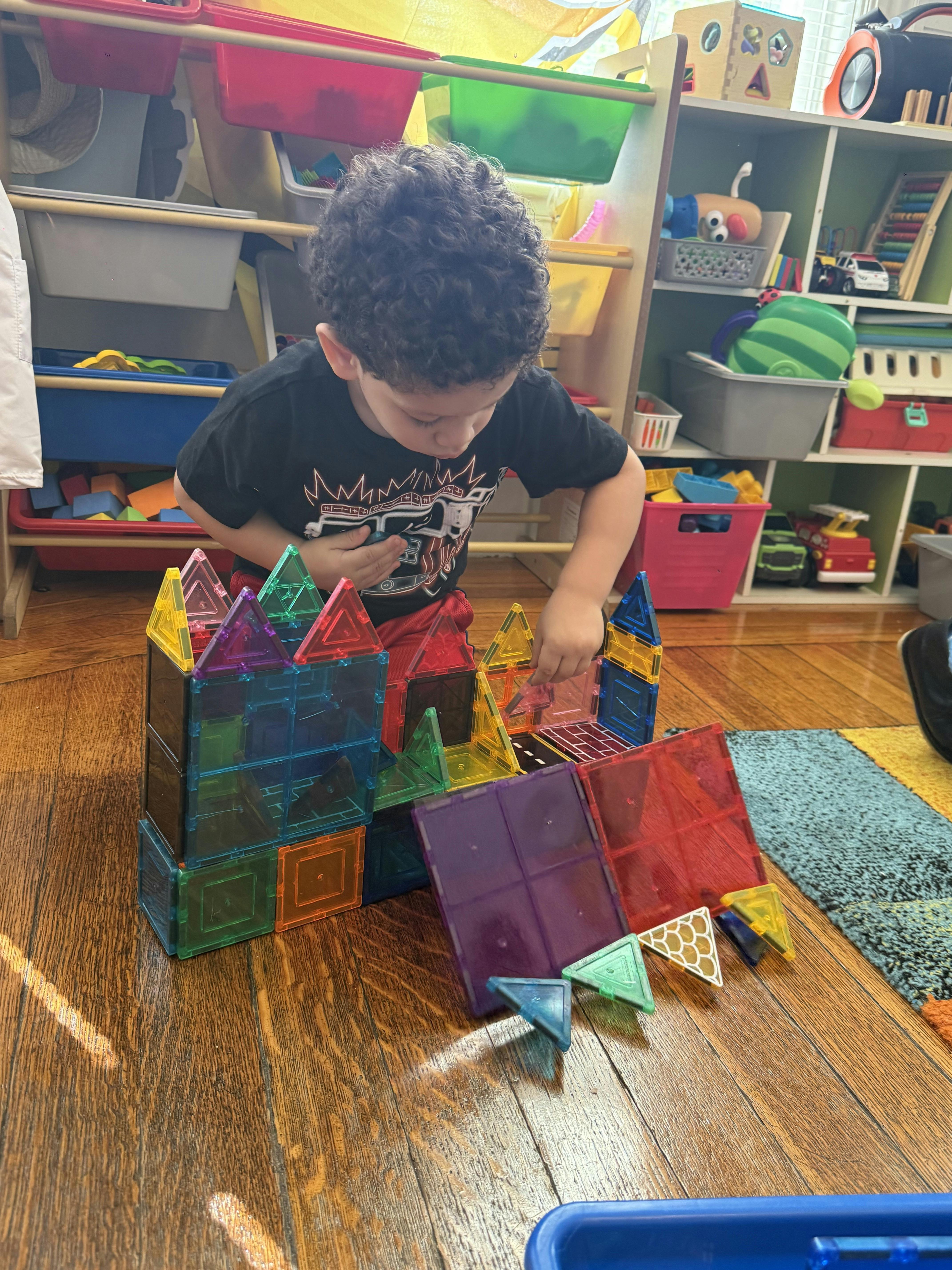 Child playing with colorful magnetic building tiles on a wooden floor