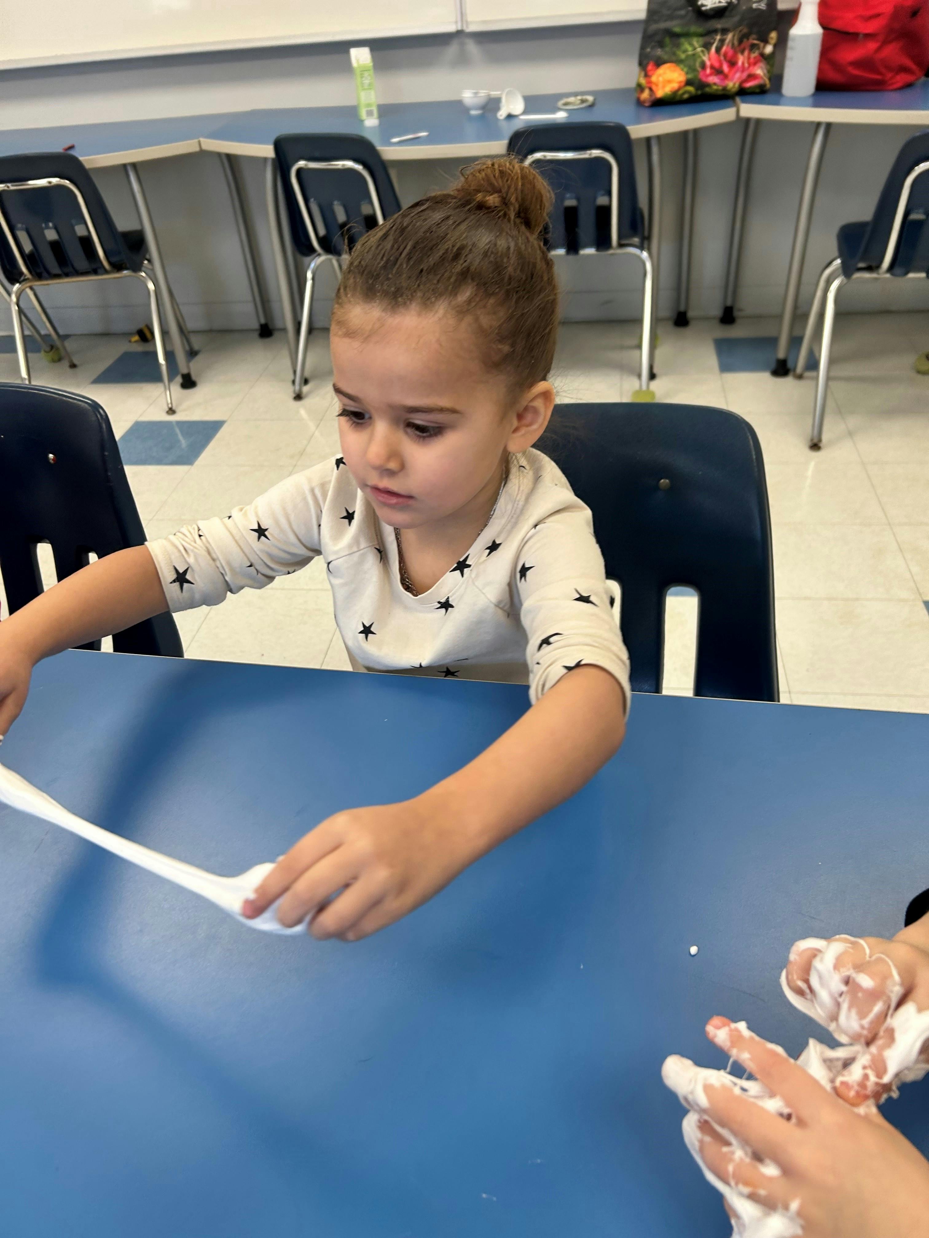 Child playing with white slime at a blue table in a classroom