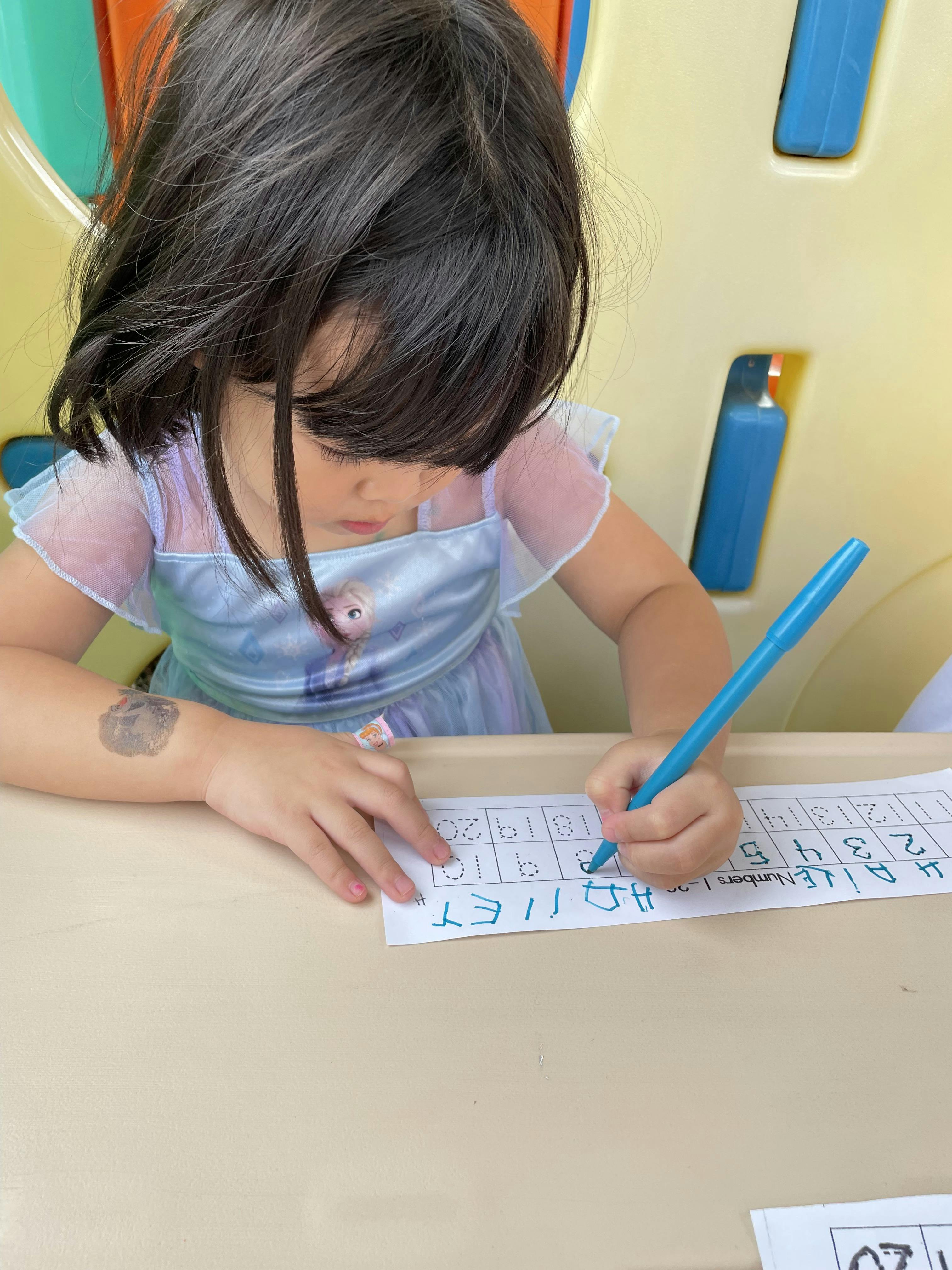 Child writing on paper with a blue pen