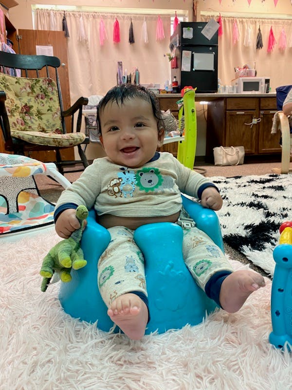 Child sitting in a blue seat holding a green toy