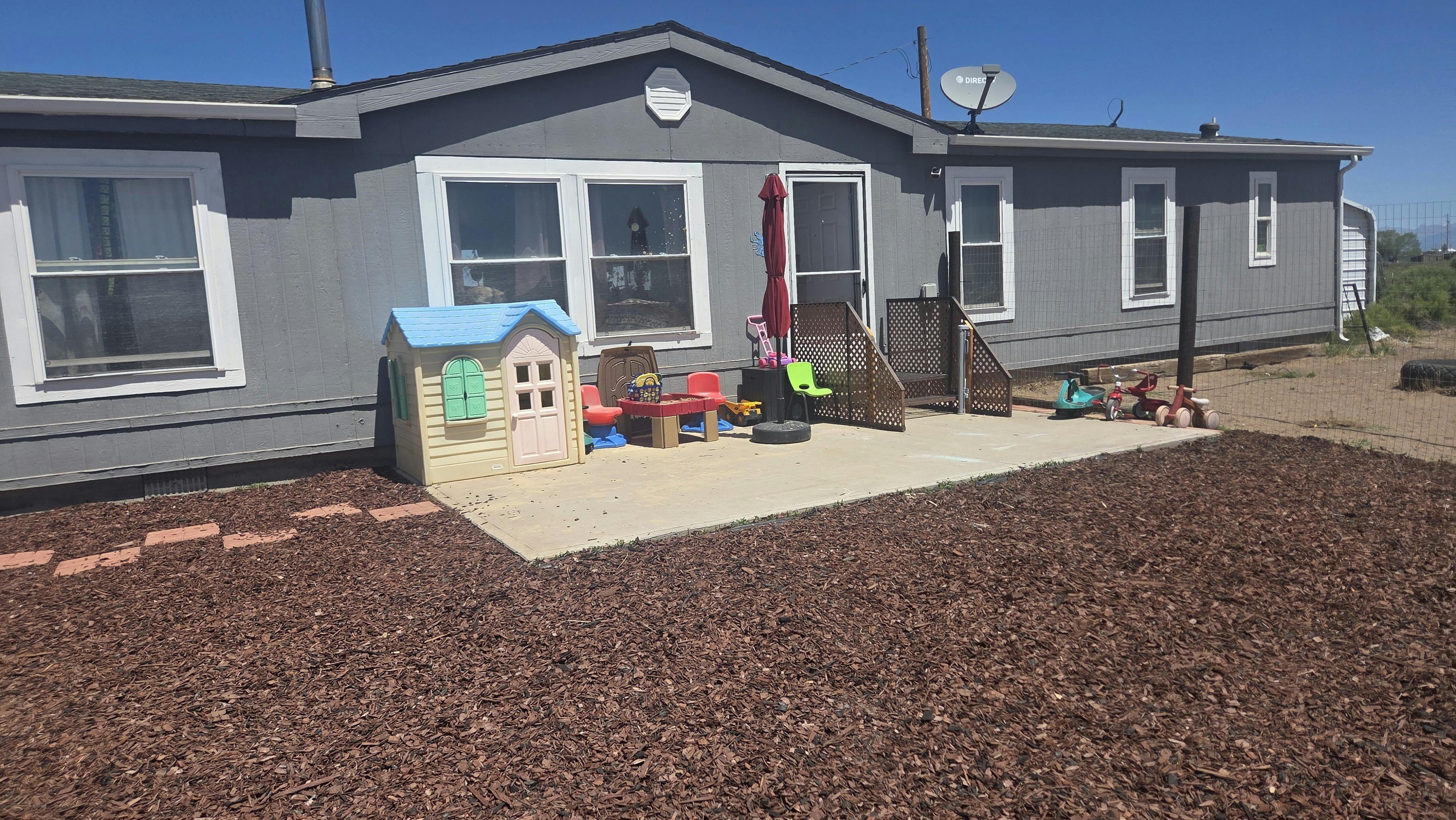 gray house with a patio, playhouse, and various child's toys
