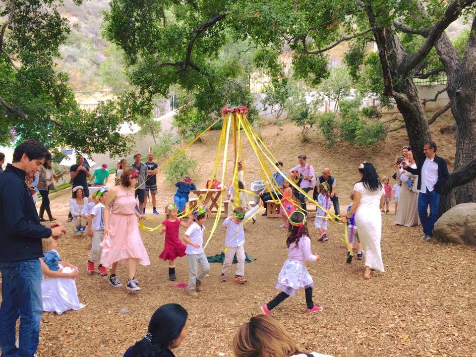 People and children dancing around a maypole outdoors